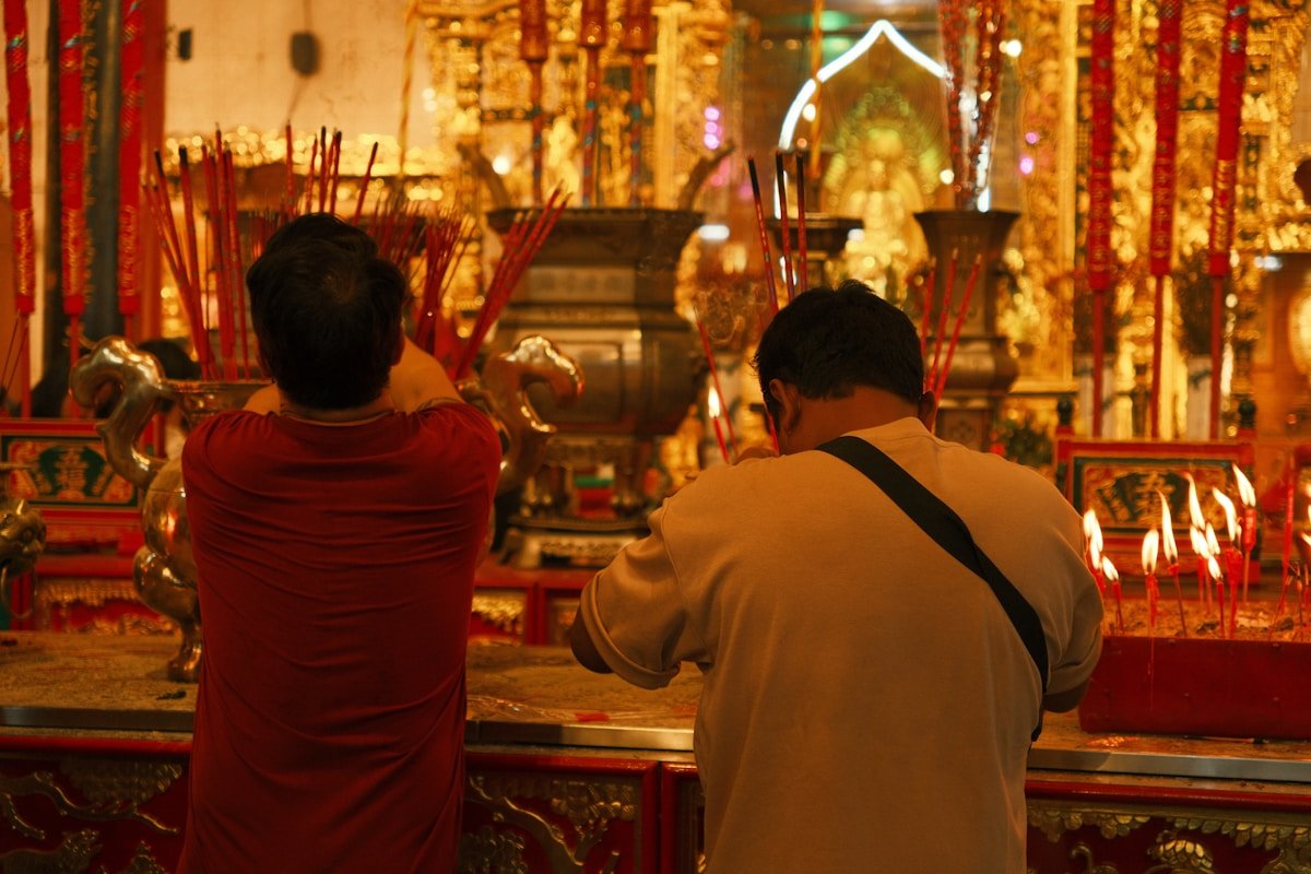 Deux hommes priant dans un temple orné de décorations dorées.