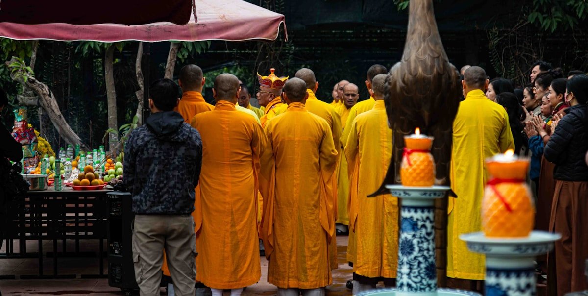 Monks in orange robes gather for a ceremony outdoors.