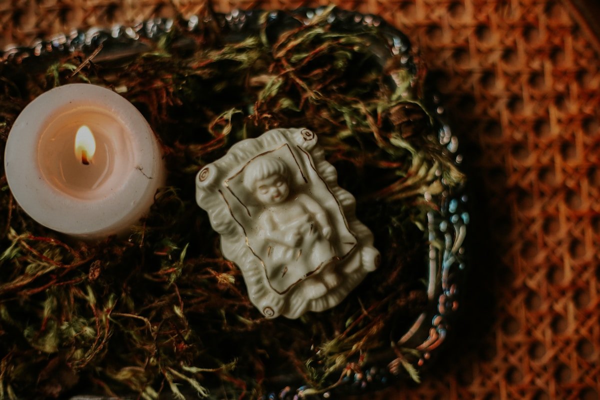 Figurine de bébé en porcelaine sur un lit de mousse et de feuilles.