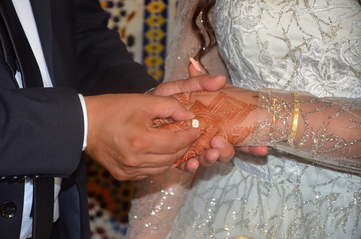 Mains jointes de mariés, robe de mariée ornée de motifs.