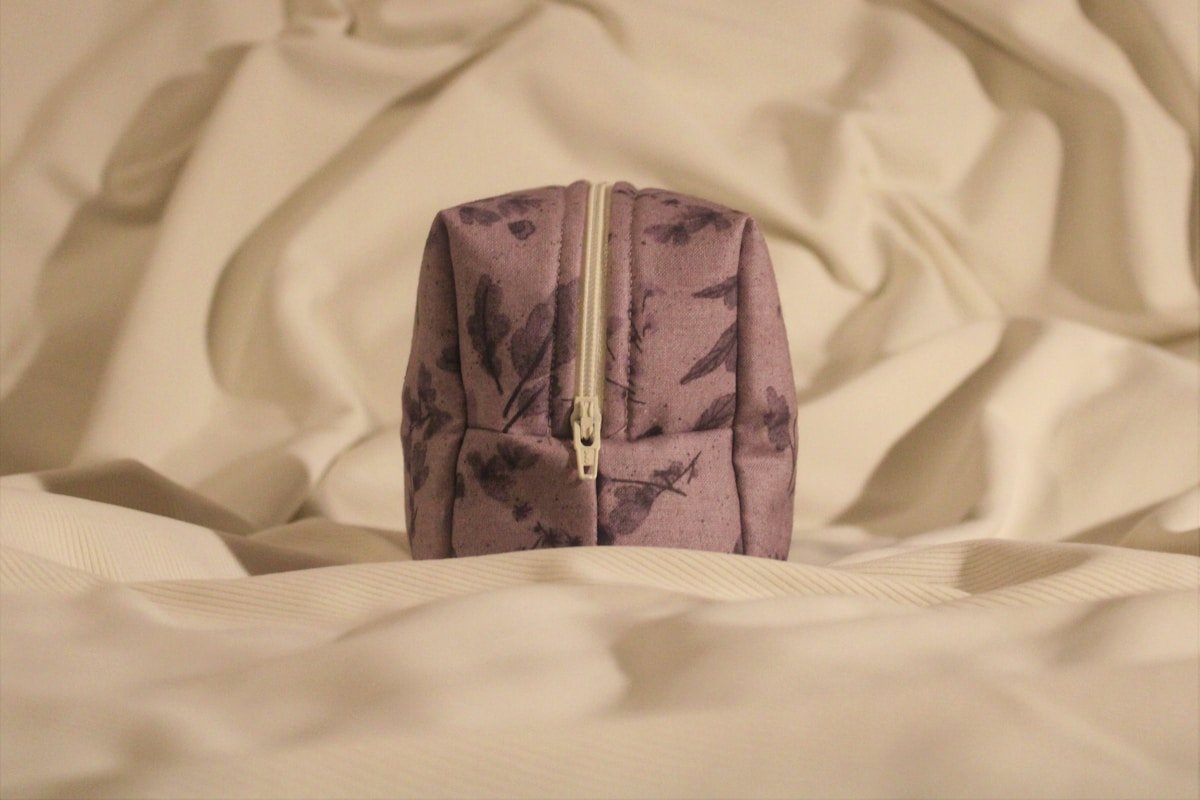 Trousse de toilette violette motifs floraux sur draps blancs.