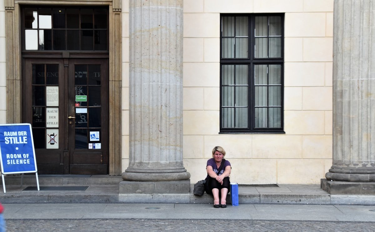 Femme assise sur les marches d'un bâtiment avec une enseigne "Raum der Stille".