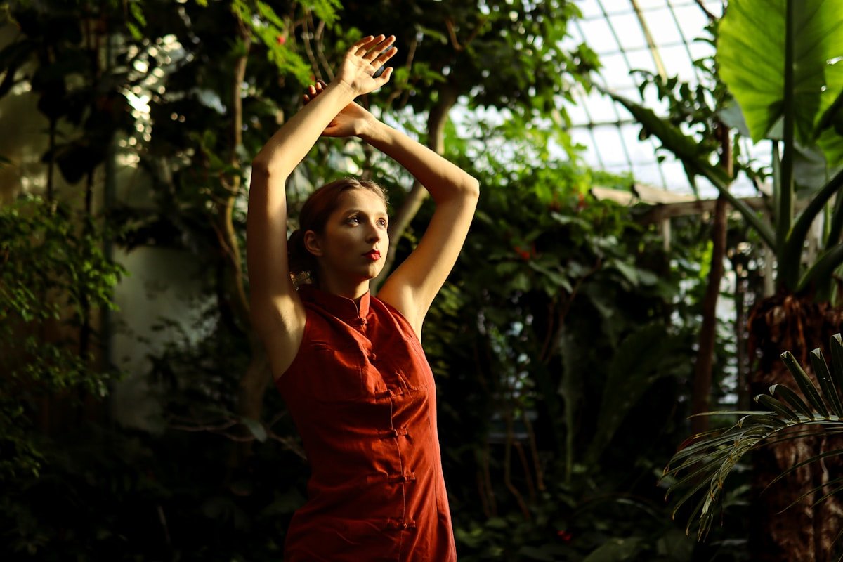 Femme en robe rouge dansant dans une serre verdoyante.